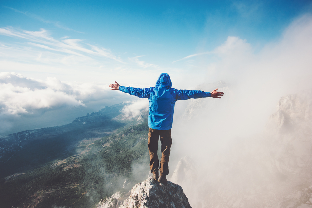 a man standing on the summit of a mountain with outstretched arms