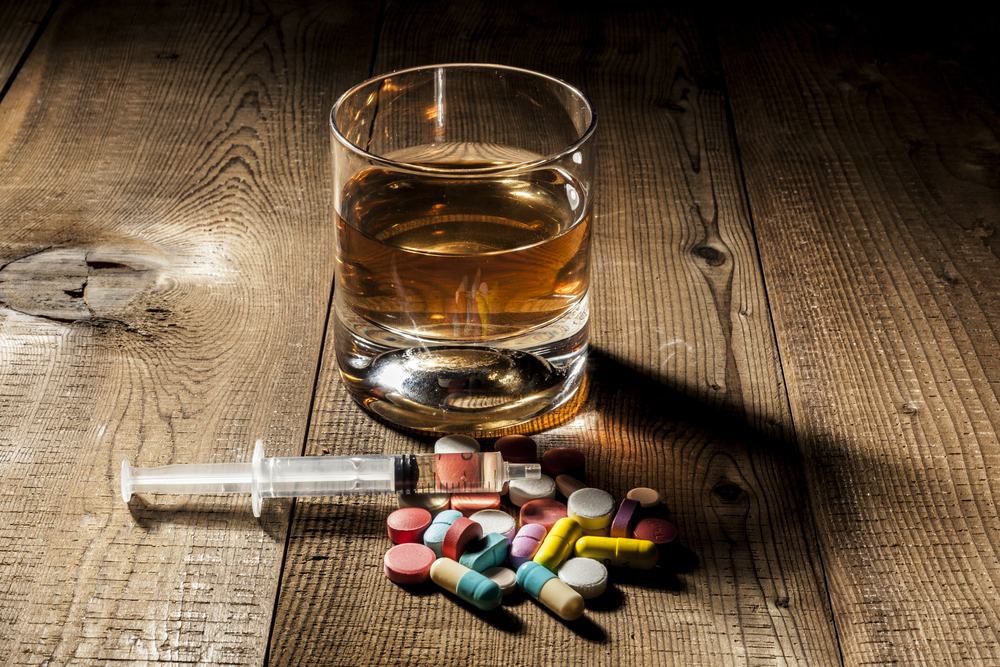 Glass of alcohol, syringe and pills on table